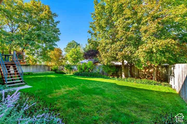 Expansive backyard featuring a grass lawn, mature trees, wood fencing, and an elevated deck with metal railings