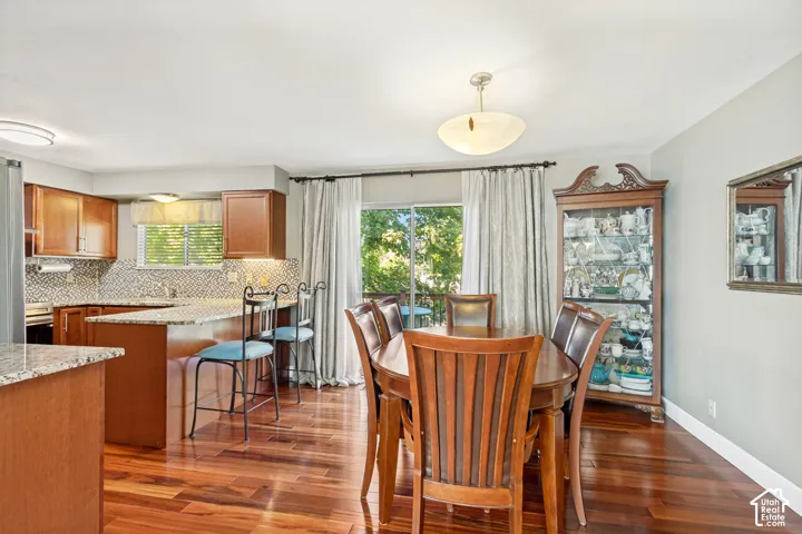 Wood-finish flooring, cherry-toned cabinetry, stone-finish countertops, geometric-patterned tile backsplash, and glass sliding door