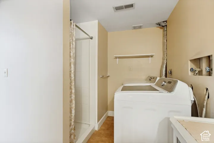 Laundry area featuring a shower stall with tile surrounds, built-in wall shelving, and utility hookups