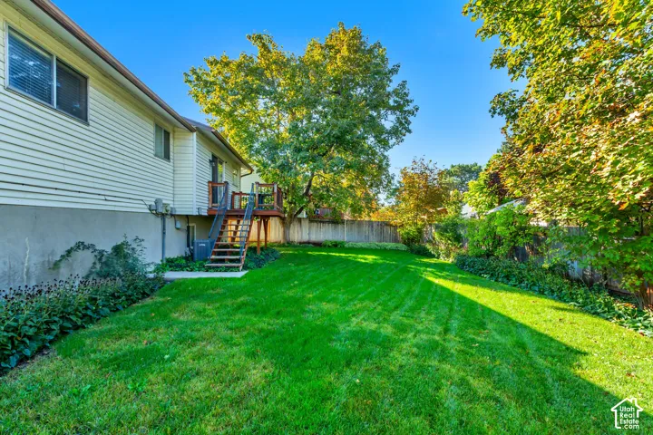Expansive backyard featuring a manicured lawn, wood deck with stairs, mature trees, and perimeter fencing