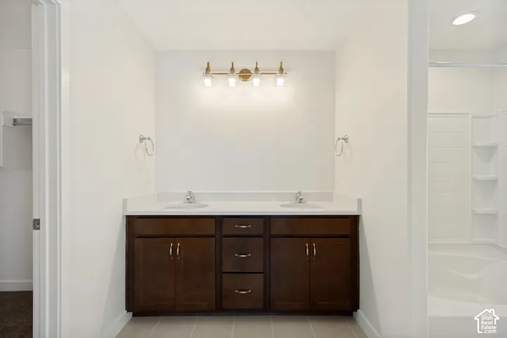 Dual-sink vanity featuring a solid surface countertop, dark wood-finish cabinetry with center drawers, four-bulb metallic light fixture, and a tub-shower combination with built-in shelving