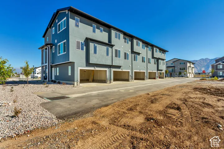 Modern multi-story exterior featuring a mix of grey stucco and vertical metal siding, multi-car garage access, and mountain backdrop
