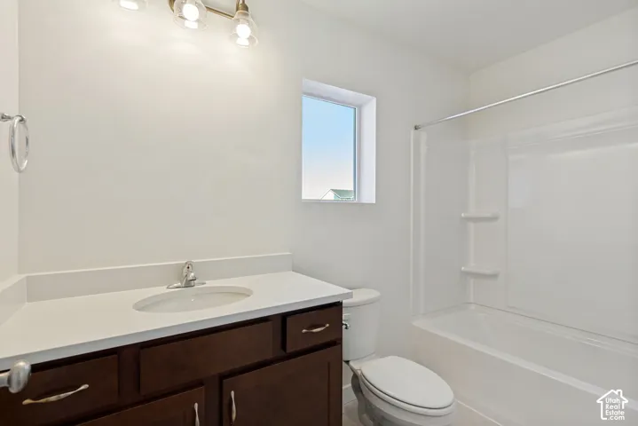 Bathroom featuring a dark wood-finish vanity with a composite countertop, integrated sink, three-light fixture, and a white tub-shower combination with built-in shelving