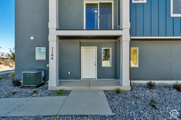 Exterior entrance featuring a concrete porch, covered portico with structural columns, vertical metal panel siding, and a sliding glass door balcony
