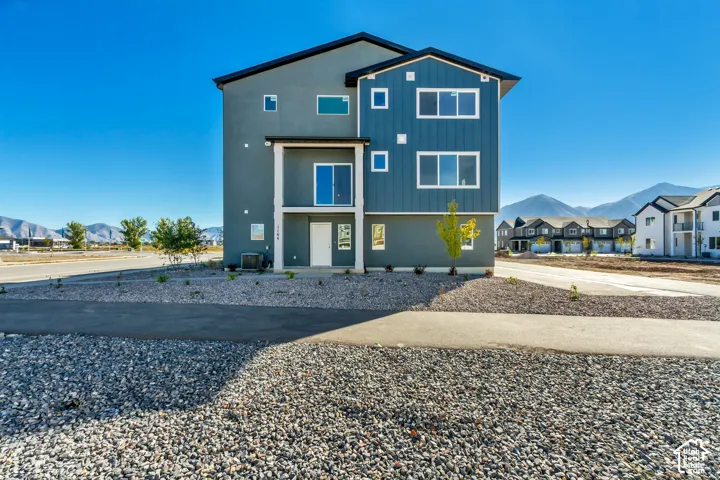 Three-story exterior featuring a mix of stucco and vertical siding, a covered entryway, and mountain backdrop
