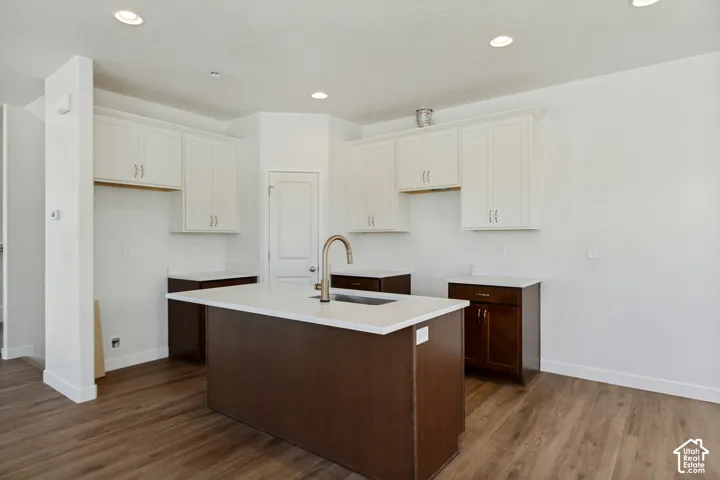 Kitchen featuring a central island with a solid-surface countertop and undermount sink, dark-finish cabinetry, white upper cabinets, and wood-finish flooring