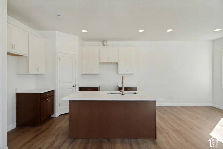 Kitchen featuring a central island with a double-basin sink, quartz countertops, two-tone cabinetry, and wood-finish flooring