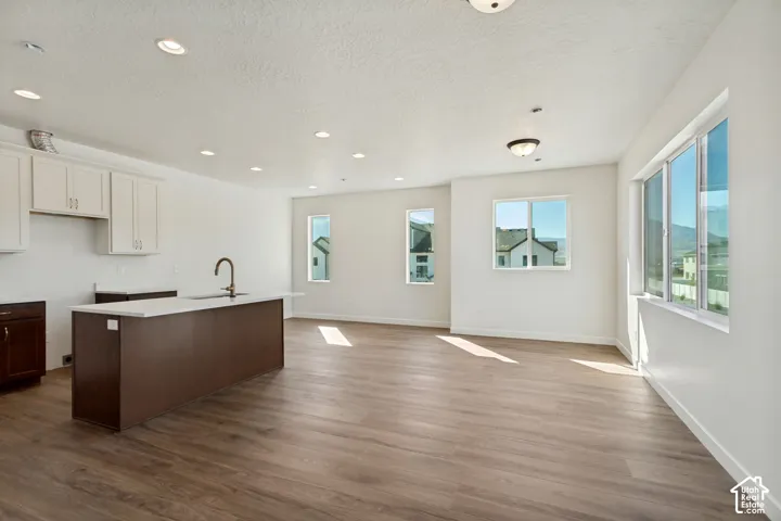 Open-concept space featuring wood-finish flooring, a kitchen island with a stone-surfaced countertop, white upper cabinetry, recessed lighting, and multiple windows