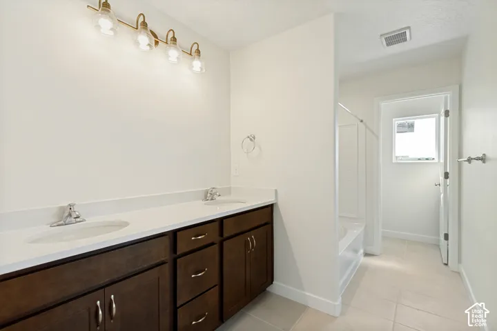 Dual-sink vanity with dark-finish cabinetry, solid-surface countertop, and multi-bulb light fixture, complemented by tiled flooring