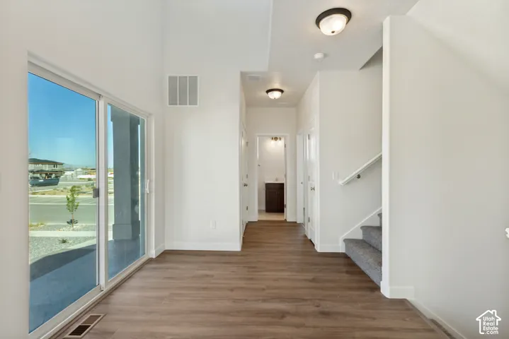 Interior featuring wood-finish flooring, vaulted ceilings, sliding glass door, and carpeted staircase with white handrail