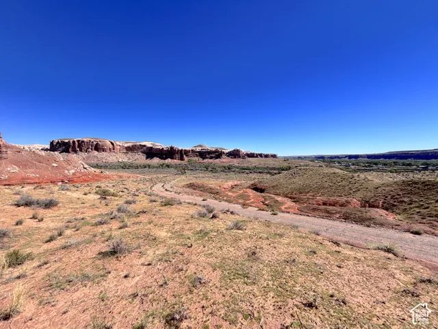 Expansive desert landscape featuring red rock mesas, rugged natural terrain, and an unpaved earthen path