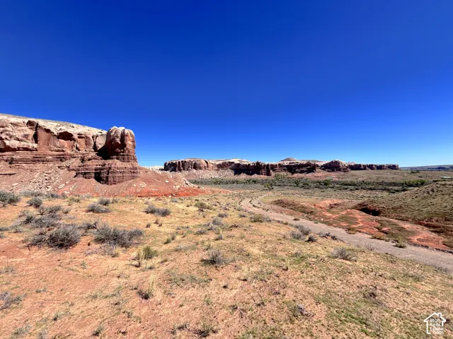 Expansive natural landscape featuring rugged sandstone rock formations, native high-desert vegetation, and an unpaved earthen path