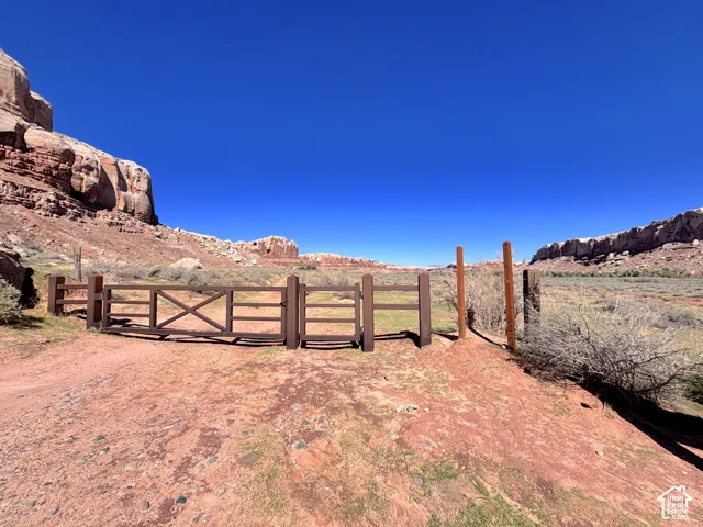 Natural landscape featuring prominent red rock formations, native brush, and a structural wood-plank gated entry