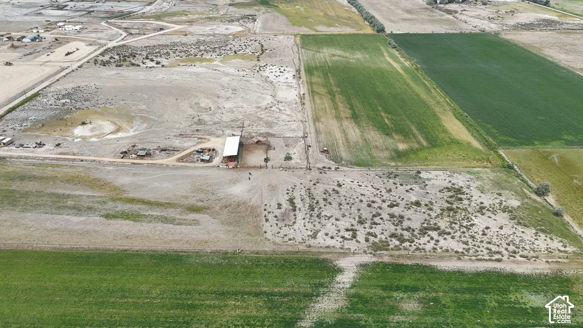 Aerial perspective of expansive acreage featuring open pasture land, dirt access roads, and a covered structure