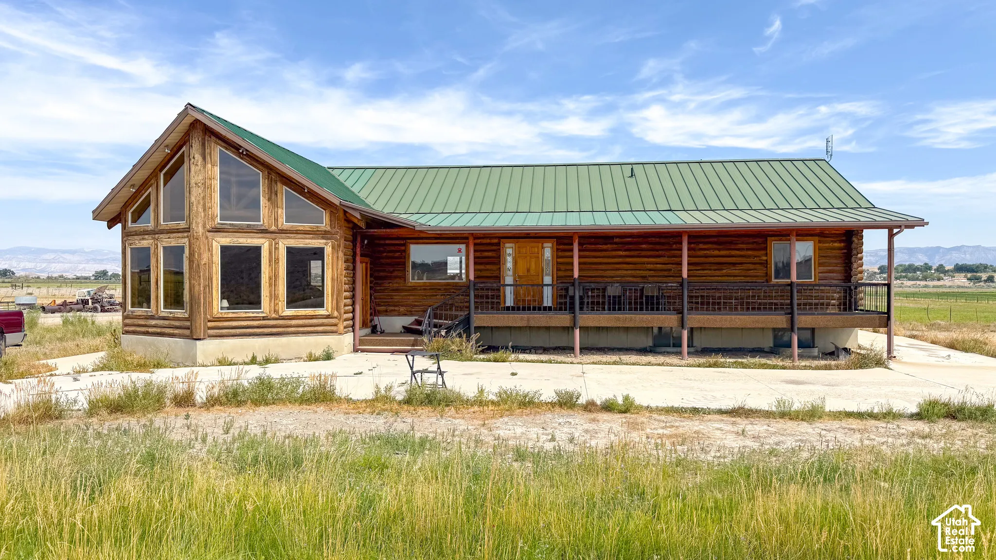 Log-construction exterior featuring a green metal roof, expansive multi-pane windows, and a covered porch with metal railing
