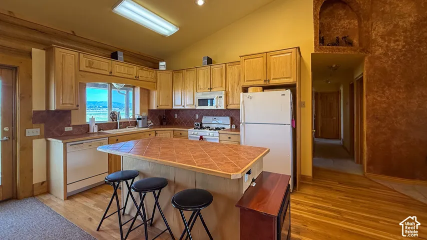 Kitchen featuring natural wood cabinetry, a central island with a tiled countertop, wood-finish flooring, vaulted ceilings, and a decorative arched wall niche