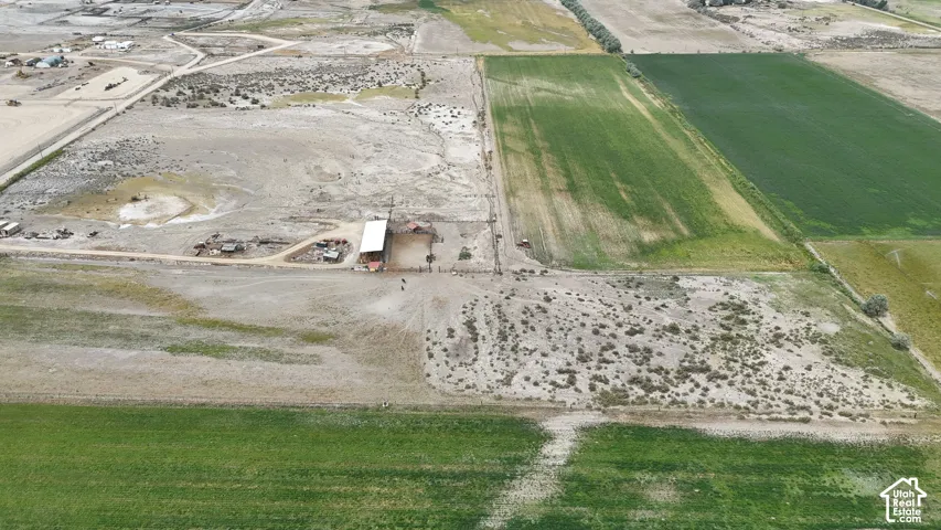 Aerial perspective of expansive acreage featuring open pasture land, dirt access roads, and a covered structure