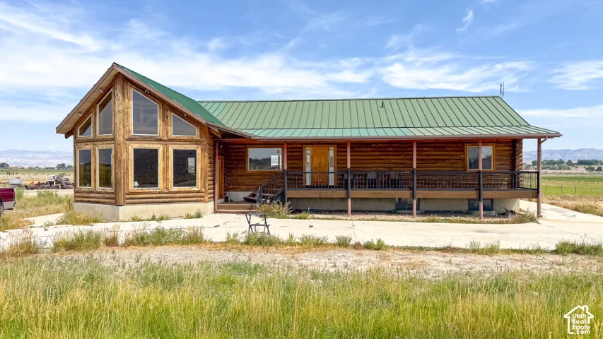 Log-construction exterior featuring a green metal roof, expansive multi-pane windows, and a covered porch with metal railing