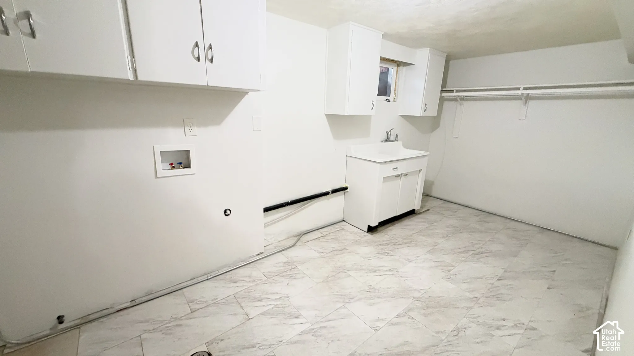 Laundry area featuring white cabinetry, a built-in utility sink with storage, stone-patterned tile flooring, and integrated wall-mounted shelving