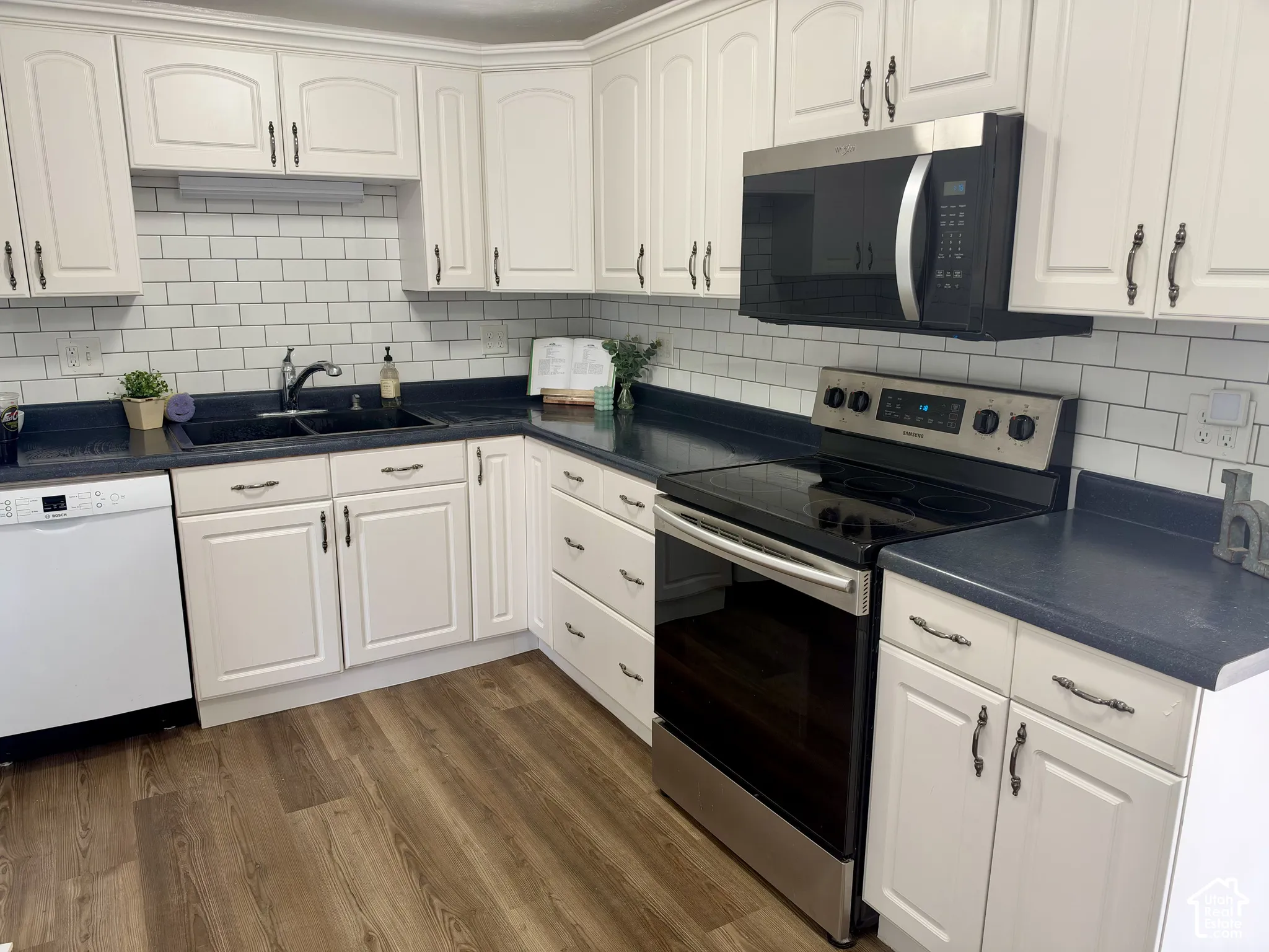 Kitchen featuring white cabinetry, subway tile backsplash, dark solid-surface countertops, wood-finish flooring, and stainless steel appliances