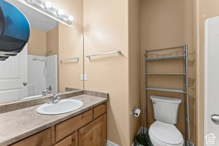 Bathroom featuring wood cabinetry, solid-surface countertop with integrated basin, full-width vanity mirror, and a combination tub and shower enclosure with tile surround