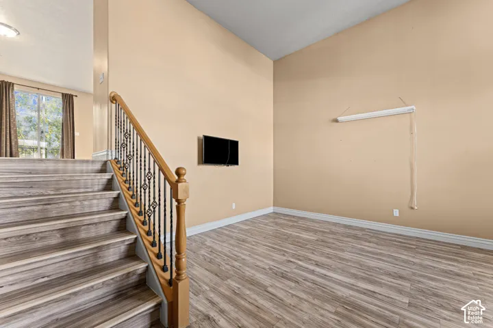 Vaulted ceiling, wood-finish flooring, and staircase featuring a wood handrail with decorative metal balusters