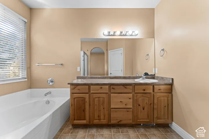 Bathroom featuring a built-in wooden vanity with an integrated countertop, a full-width wall mirror, a multi-bulb light fixture, and a tiled soaking tub