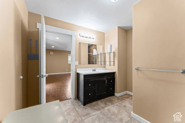 Dark-finished vanity with a white countertop and integrated sink, rectangular frameless mirror, chrome wall-mounted light fixture, and tile flooring