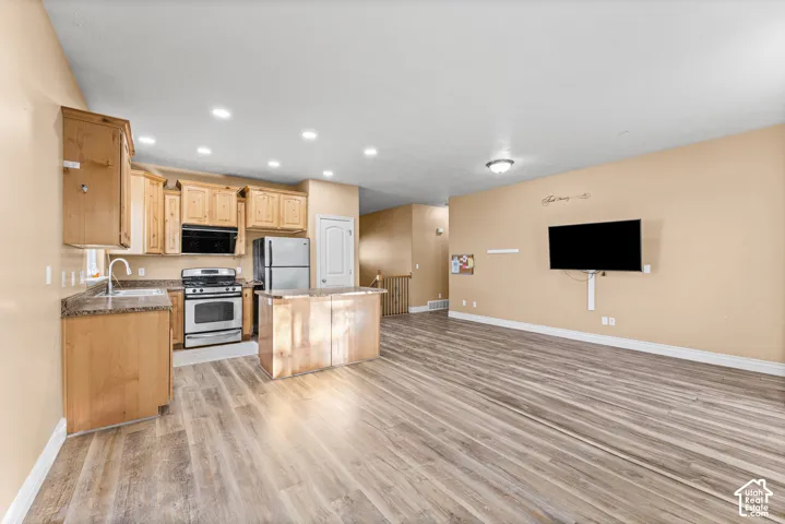 Kitchen area featuring light-finish cabinetry, a center island with stone-finish countertops, stainless steel appliances, and wood-finish flooring