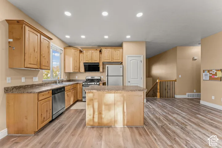 Kitchen featuring natural-finish wood cabinetry, a center island, stone-patterned laminate countertops, stainless steel appliances, and wood-finish flooring
