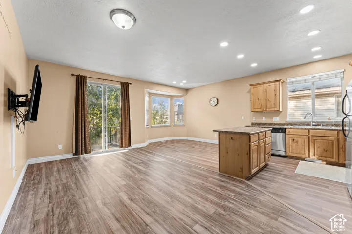 Wood-finish flooring, kitchen island with stone-surface countertop, natural wood cabinetry, bay window, and sliding glass patio door