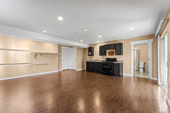 Open floor plan featuring wood-finish flooring, recessed lighting, built-in wall shelving, dark cabinetry with a range, and sliding glass doors