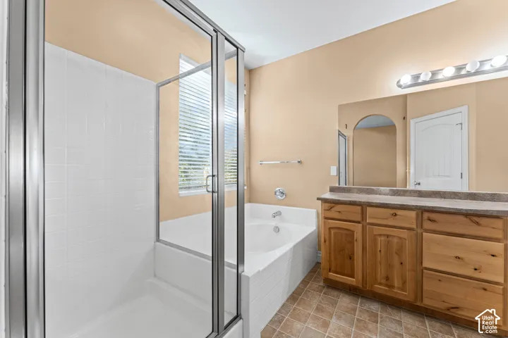 Bathroom featuring a glass-enclosed shower, a tiled soaking tub, natural wood-finish cabinetry, a solid-surface vanity countertop, and ceramic tile flooring