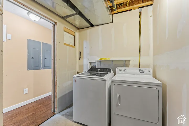 Utility area featuring unfinished drywall, exposed metal ductwork, wood-finish flooring in the threshold, dual electrical service panels, and washer and dryer hookups