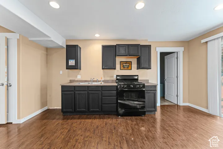 Kitchenette featuring dark-finish cabinetry, solid-surface countertops, integrated gas range, recessed ceiling lighting, and wood-finish flooring