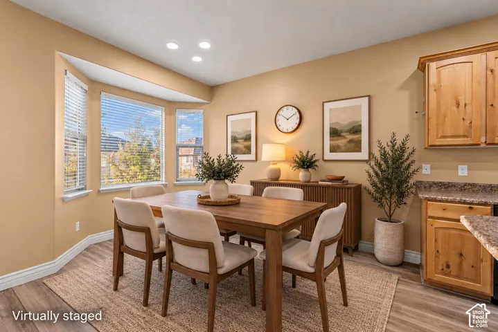 Bay window with horizontal blinds, wood-finish flooring, and natural wood cabinetry with stone-finish countertops