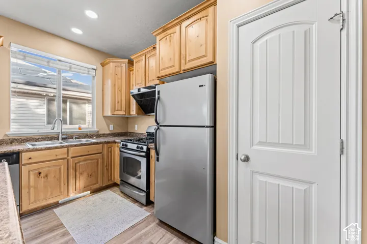 Kitchen featuring natural wood-finish cabinetry, stone-texture countertops, stainless steel appliances, recessed ceiling lighting, and a double-basin stainless steel sink