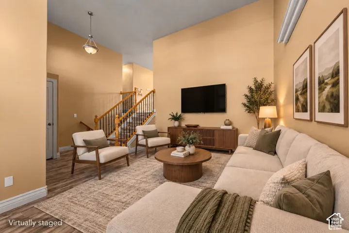 Vaulted ceiling, open-concept living area, wood-finish flooring, and a staircase featuring wood handrails with metal balusters
