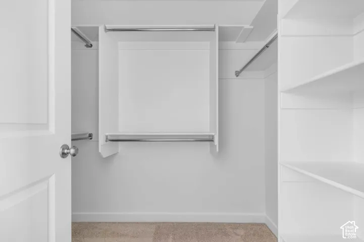 Walk-in closet featuring white built-in shelving, integrated tiered clothing rods, and wall-to-wall carpeting