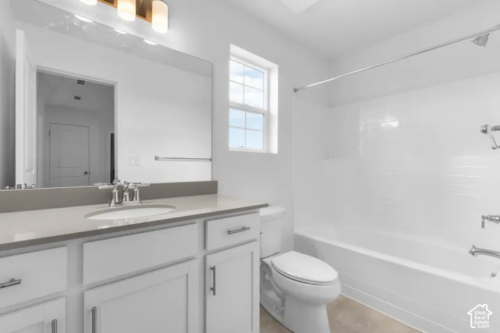 Bathroom featuring a white vanity with a neutral solid-surface countertop, an integrated sink, full-width wall mirror, subway-tiled tub surround, and polished chrome fixtures