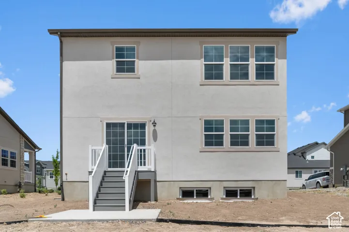 Stucco exterior featuring dual-level grid windows, a concrete ground-level patio, and a staircase with white railings leading to a sliding glass door