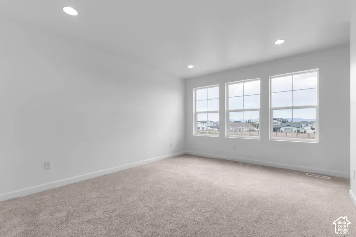 Neutral-toned carpeted flooring, recessed lighting, and three tall grid-pattern windows