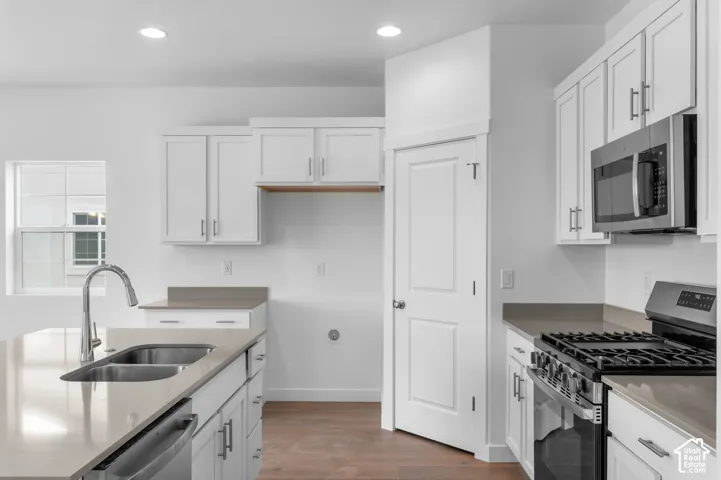 Kitchen featuring white Shaker-style cabinetry, neutral-toned solid surface countertops, a stainless steel dual-basin undermount sink with a gooseneck faucet, a built-in stainless steel microwave, and wood-finish flooring