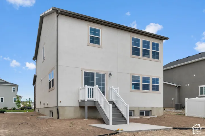 Two-story exterior featuring light-toned siding, a rear deck with white railing, a concrete patio, and a sliding glass door