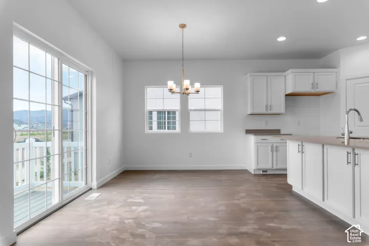 Dining area featuring wood-finish flooring, white cabinetry, a neutral solid-surface countertop, an overhead chandelier, and sliding glass doors
