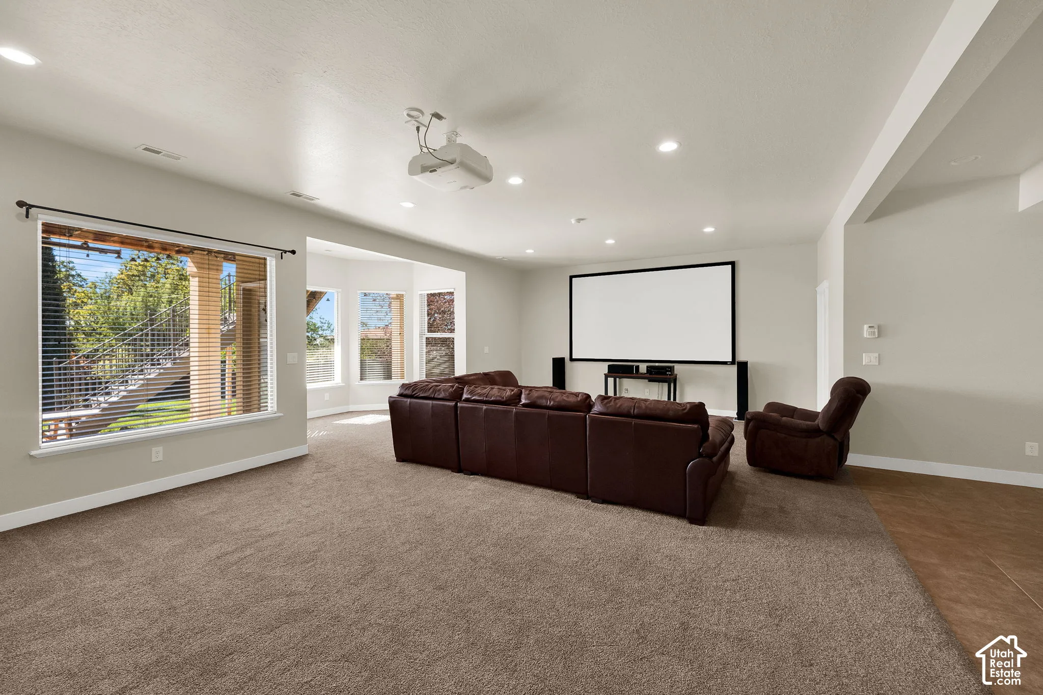 Recessed lighting, ceiling-mounted projector, wall-mounted projection screen, expansive windows, and carpeted flooring