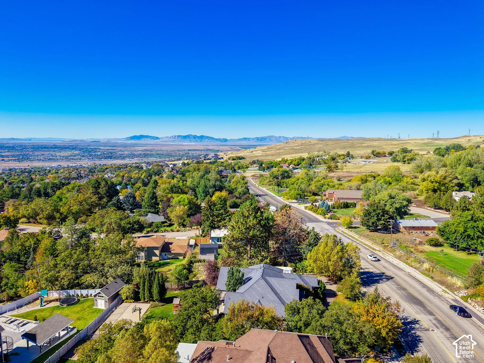 Aerial perspective of the property featuring a multi-pitched roof, manicured lawn, paved driveway, and expansive mountain range scenery