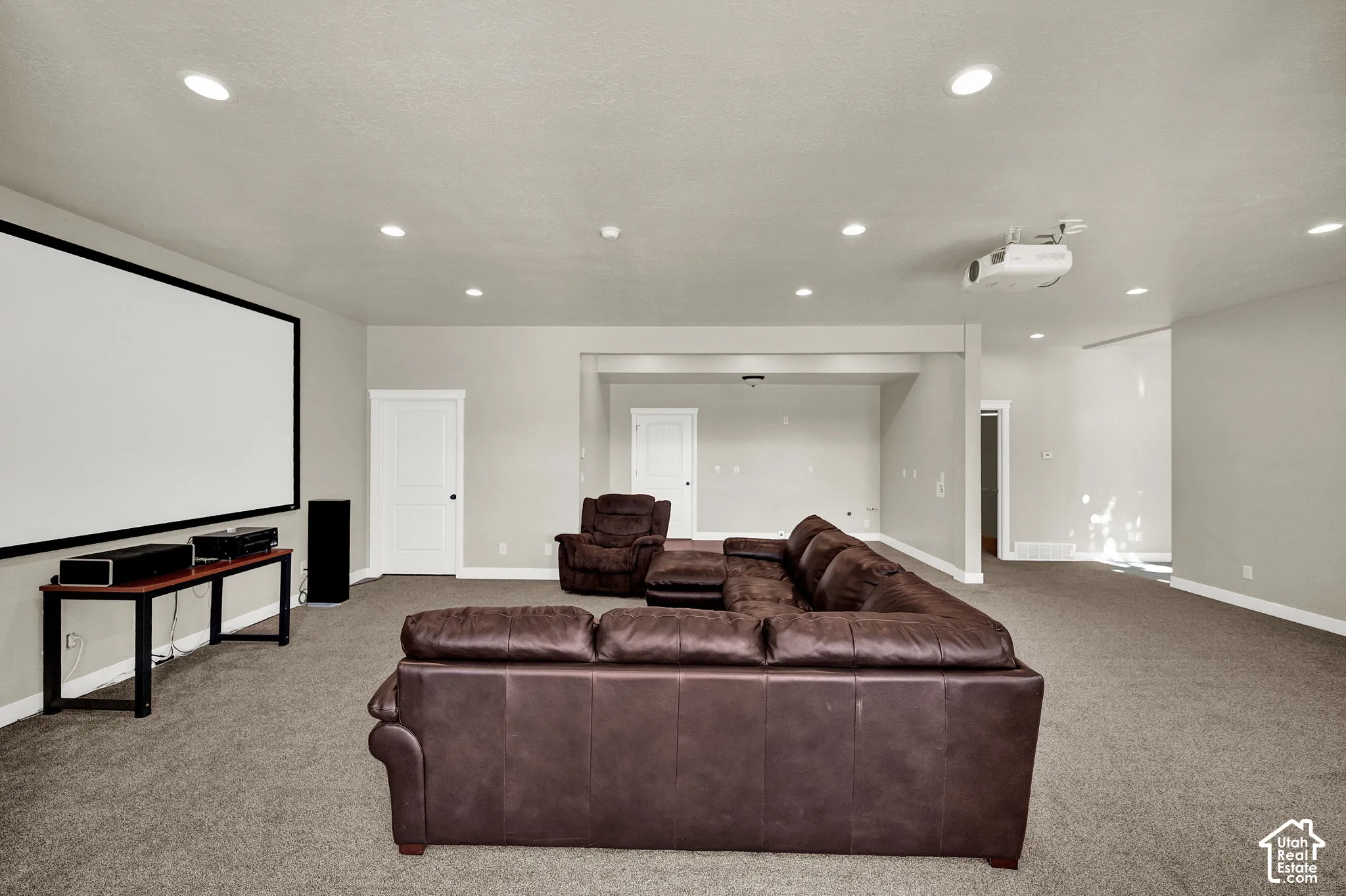 Large multipurpose room featuring neutral wall-to-wall carpeting, recessed ceiling lighting, a wall-mounted projection screen, and a ceiling-mounted projector