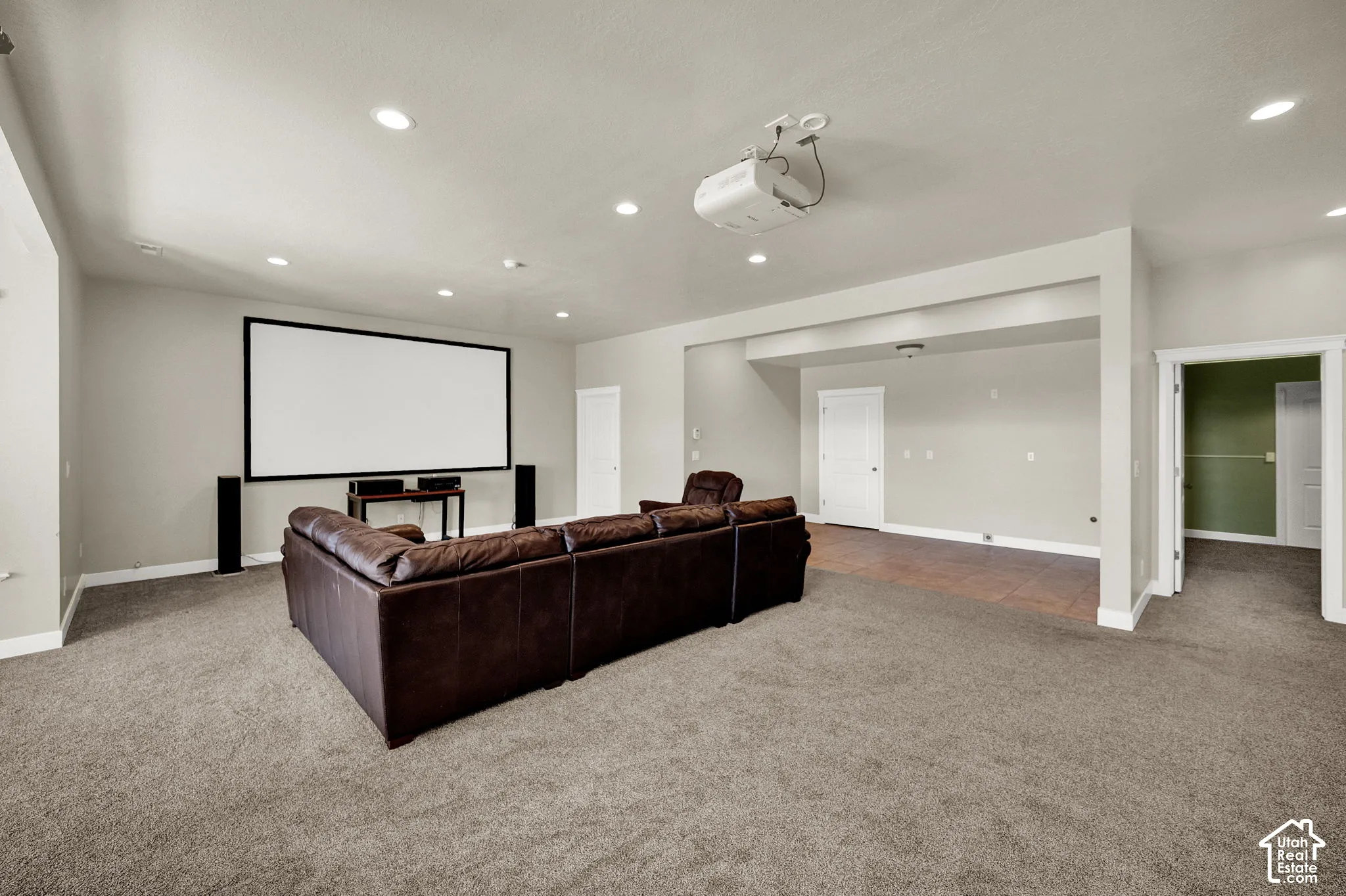 Large room featuring recessed lighting, a ceiling-mounted projector, wall-mounted projection screen, carpeting, and a tiled alcove
