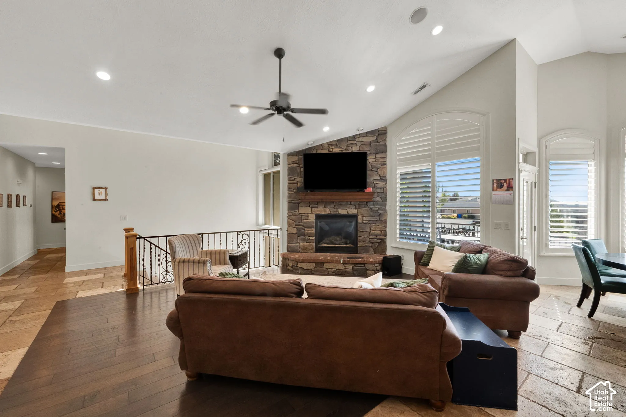 Vaulted ceilings with recessed lighting, stone-clad fireplace with a wood mantel, stone tile flooring, dark wood-finish flooring, and arched windows with plantation shutters